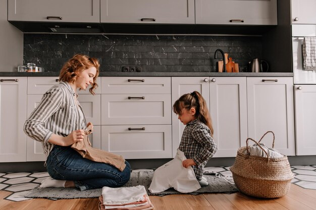 Encantadora mujer y su hija están sentadas en la cocina y poniendo tshir lavado