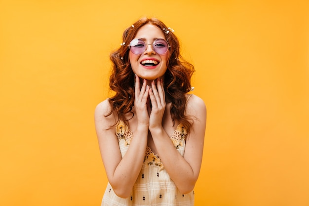 Encantadora mujer vestida con top a cuadros se ríe. Foto de mujer pelirroja con gafas color lila.