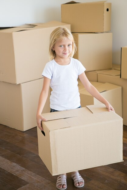 Encantadora niña llevando caja de cartón y mirando a cámara