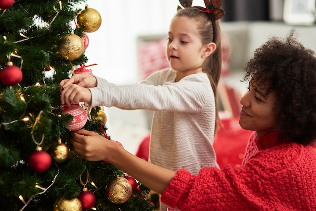 Encantadora niña y mamá decorando el árbol de Navidad