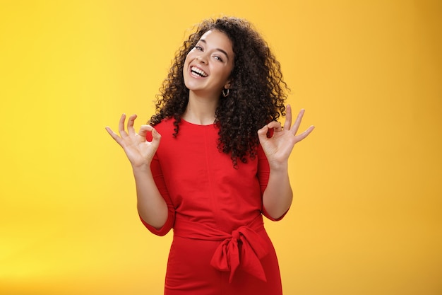 Encantadora niña que vive el sueño de pie feliz y satisfecho como si le gustara el alquiler de un apartamento nuevo con su novio mostrando un gesto bien e inclinando la cabeza con una amplia sonrisa aprobando un lugar fresco sobre fondo amarillo.