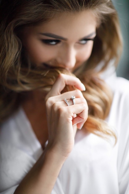 Foto gratuita encantadora novia rubia con rizos y piel brillante posa en bata de seda blanca en la habitación