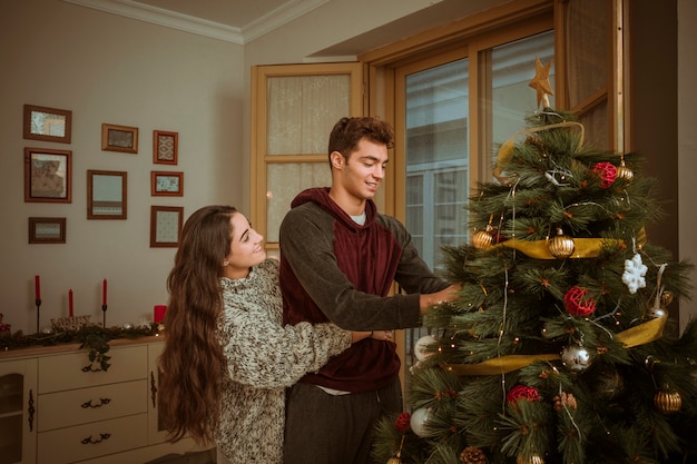 Encantadora pareja abrazándose mientras decoraba el árbol de navidad