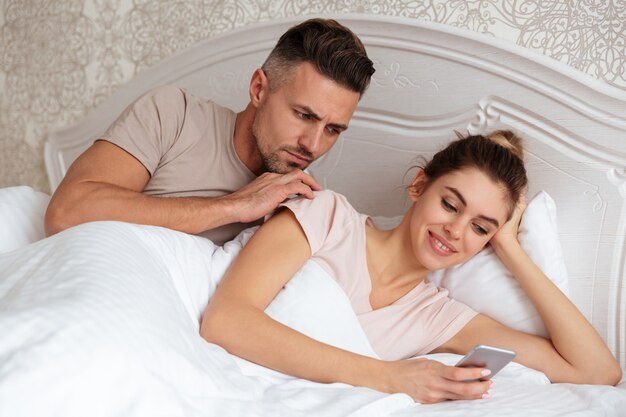 Encantadora pareja acostada juntos en la cama mientras la mujer usa el teléfono inteligente