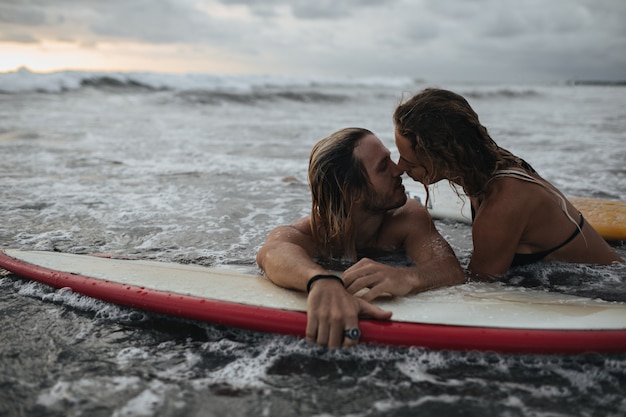 Encantadora pareja besándose durante el atardecer en la tabla de surf