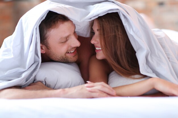 Encantadora pareja en la cama debajo de las sábanas.