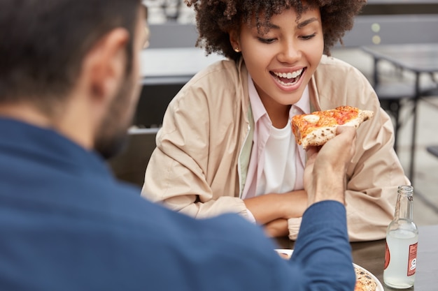 Foto gratuita encantadora pareja come pizza en la cafetería al aire libre