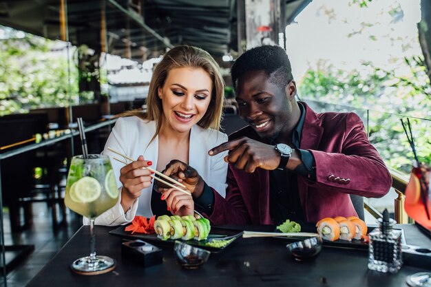 Encantadora pareja divirtiéndose mientras come sushi rolls en restaurante en terraza moderna.