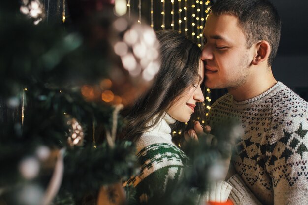 La encantadora pareja de enamorados abrazándose cerca de árbol de Navidad