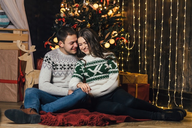 La encantadora pareja de enamorados sentados cerca del árbol de Navidad