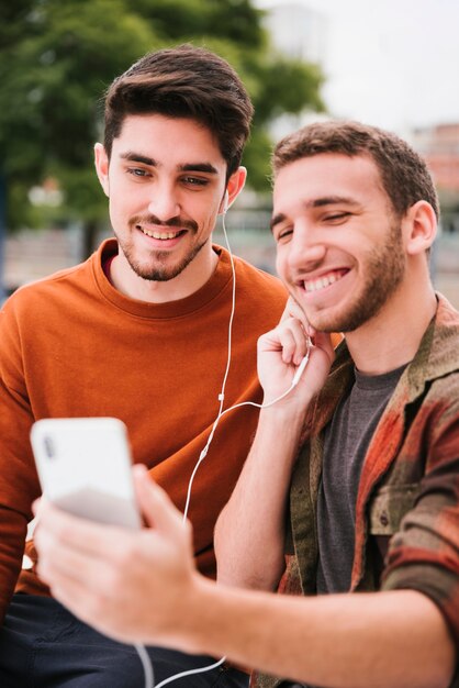 Encantadora pareja gay en auriculares escuchando música en el móvil