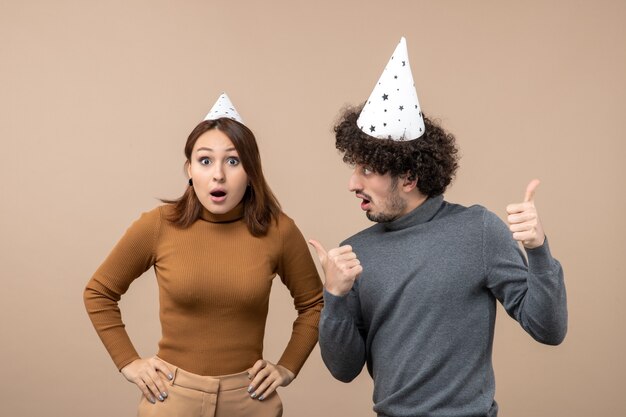 Encantadora pareja joven emocionada usa sombrero de año nuevo niña sorprendida de pie cerca de chico en imagen gris