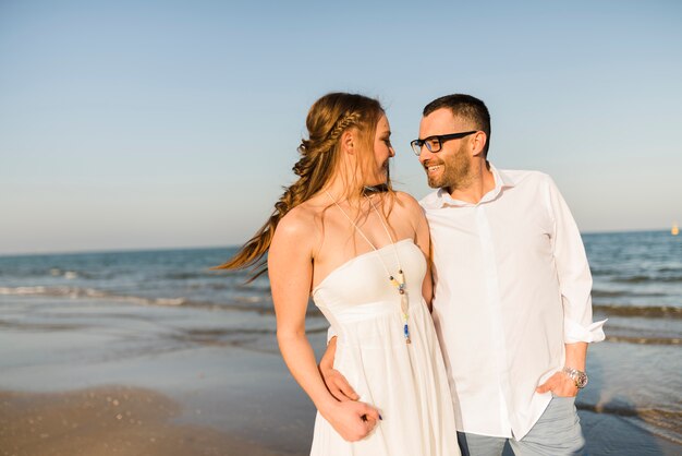 Encantadora pareja joven de pie cerca de la orilla del mar en la playa