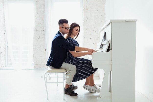 Encantadora pareja joven tocando el piano juntos en casa