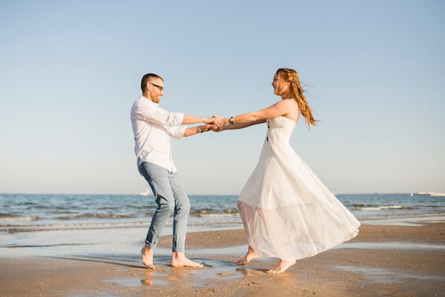 Encantadora pareja de jóvenes bailando juntos cerca de la costa en la playa