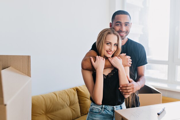 Encantadora pareja en movimiento, comienzo de una nueva vida en casa, piso, hombre abraza a su dama en apartamento entre cajas