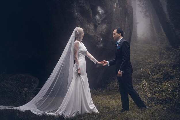 Encantadora pareja de recién casados - novia y novio en un hermoso bosque misterioso con una asombrosa niebla otoñal.