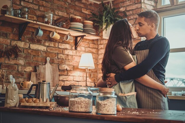 Encantadora pareja romántica se besa en la cocina mientras prepara el desayuno.