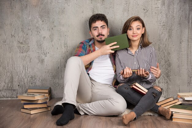 Encantadora pareja sentada en el suelo y sosteniendo libros