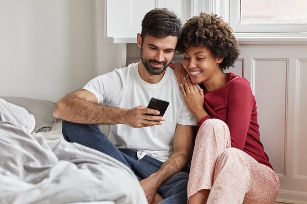 Encantadora pareja se sienta en el piso cerca de la cama y disfruta del ambiente doméstico