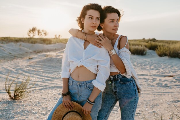 Encantadoras dos mujeres jóvenes divirtiéndose en la playa al atardecer, romance de amor lesbiana gay