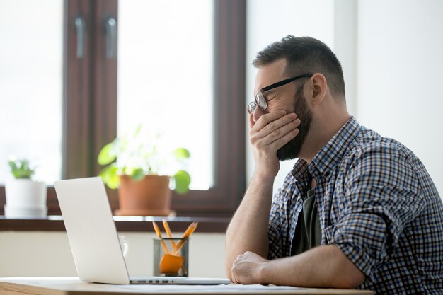 Encargado soñoliento cansado en los vidrios que bostezan en el trabajo en oficina