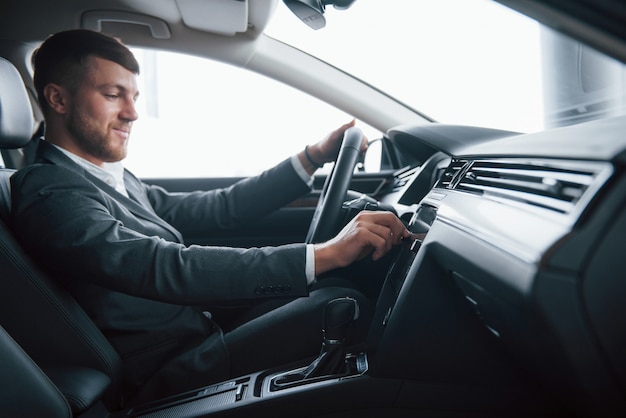 Enciende la música. Hombre de negocios moderno probando su nuevo coche en el salón del automóvil