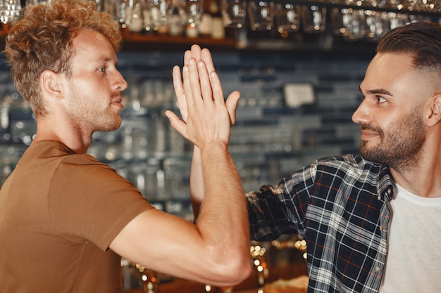 Encuentro con los mejores amigos. Dos hombres jóvenes felices en ropa casual hablando y bebiendo cerveza mientras están sentados juntos en el bar.