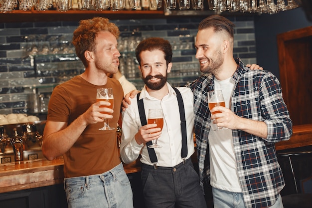 Foto gratuita encuentro con los mejores amigos. tres hombres jóvenes felices en ropa casual hablando y bebiendo cerveza mientras están sentados juntos en el bar.