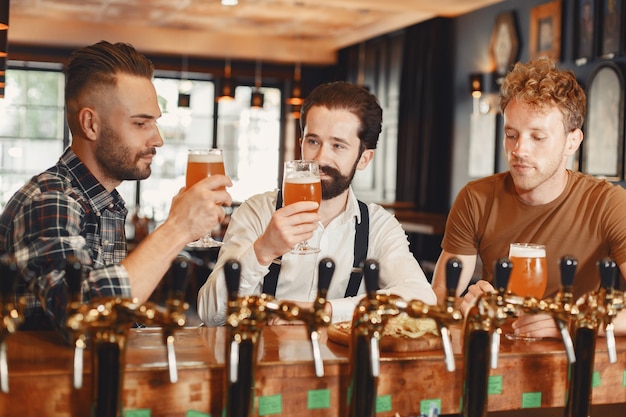 Encuentro con los mejores amigos. Tres hombres jóvenes felices en ropa casual hablando y bebiendo cerveza mientras están sentados juntos en el bar.