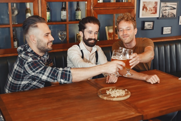 Foto gratuita encuentro con los mejores amigos. tres hombres jóvenes felices en ropa casual hablando y bebiendo cerveza mientras están sentados juntos en el bar.