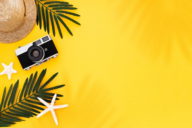 Endecha plana con accesorios para viajeros: hoja de palma tropical, cámara retro, sombrero para el sol, estrellas de mar sobre fondo amarillo