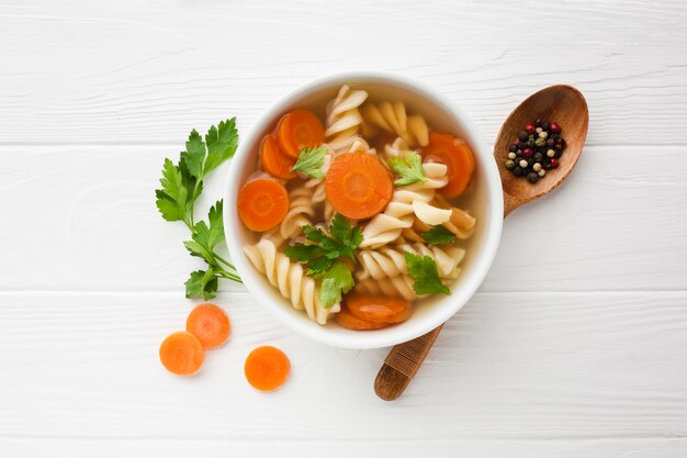 Endecha plana brócoli fusilli y zanahorias en un tazón con cuchara de madera