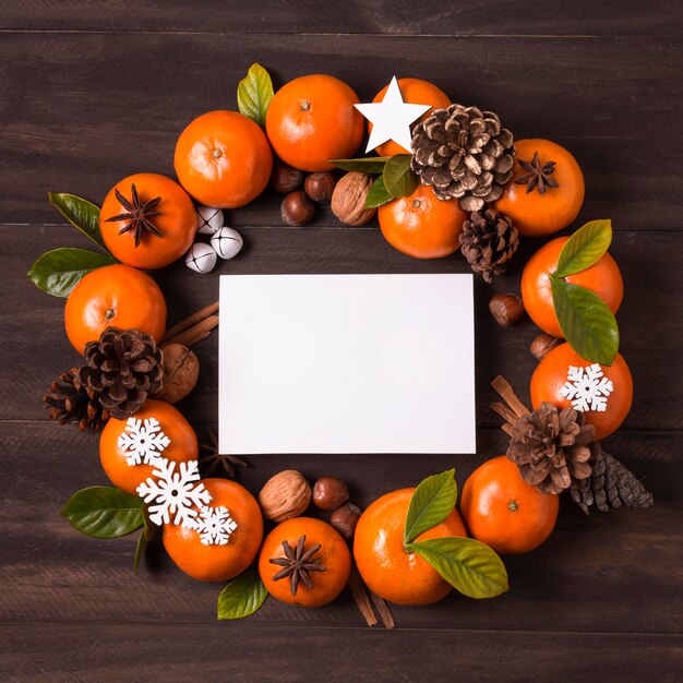 Endecha plana de corona de navidad de mandarinas y piñas con papel en blanco