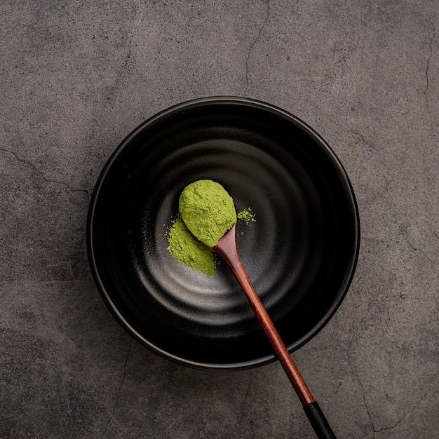 Endecha plana de cuchara de madera en un tazón con polvo de té matcha