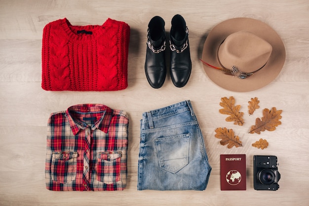 Endecha plana de estilo y accesorios de mujer, suéter de punto rojo, camisa a cuadros, jeans, botas de cuero negro, sombrero, tendencia de moda de otoño, vista desde arriba, cámara de fotos vintage, pasaporte