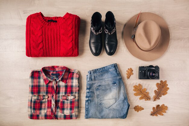 Endecha plana de estilo y accesorios de mujer, suéter de punto rojo, camisa a cuadros, jeans, botas de cuero negro, sombrero, tendencia de moda de otoño, vista desde arriba, cámara de fotos vintage, traje de viajero