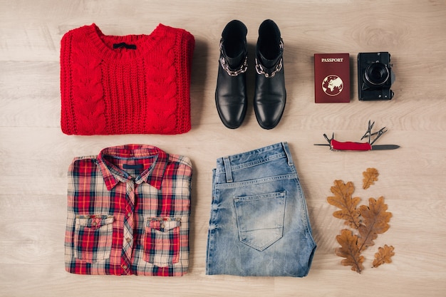 Endecha plana de estilo y accesorios de mujer, suéter de punto rojo, camisa a cuadros, jeans, botas de cuero negro, tendencia de moda de otoño, cámara de fotos vintage, cuchillo suizo, pasaporte, traje de viajero