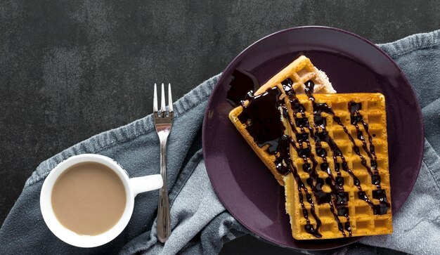 Endecha plana de gofres cubiertos de chocolate en un plato con tenedor y café