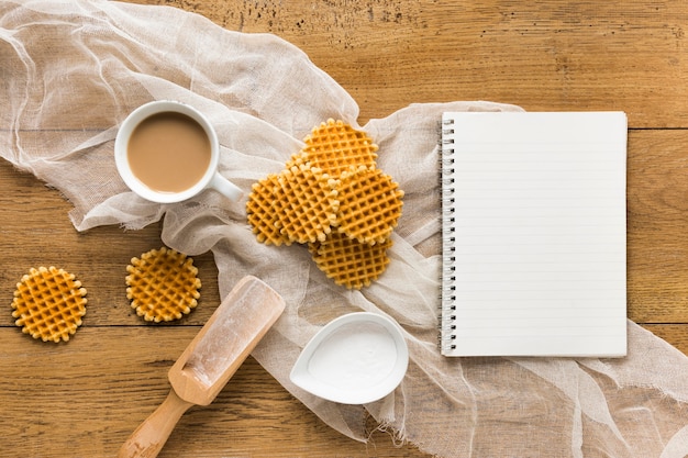 Endecha plana de gofres redondos sobre superficie de madera con cuaderno y café