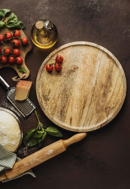 Endecha plana de masa de pizza con tablero de madera y tomates