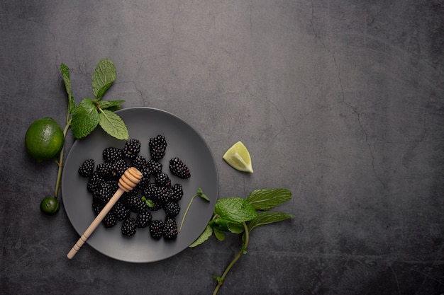 Endecha plana de moras en un plato con limas y cucharón de miel