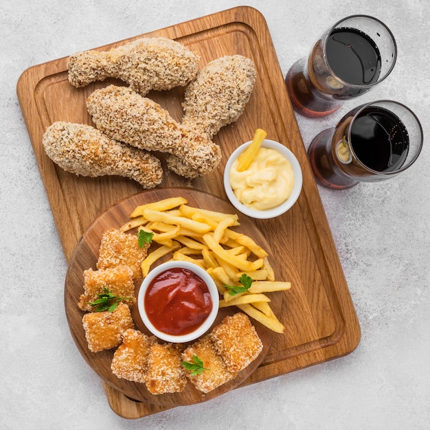 Foto gratuita endecha plana de patas de pollo frito y nuggets con bebidas gaseosas y papas fritas