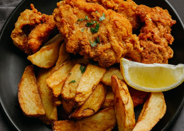 Endecha plana de pescado y patatas fritas en un plato con una rodaja de limón