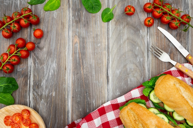 Endecha plana de sándwiches con tomates y cubiertos.