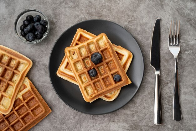 Endecha plana de waffles en un plato con arándanos y cubiertos