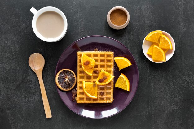 Endecha plana de waffles en un plato con cítricos y café.