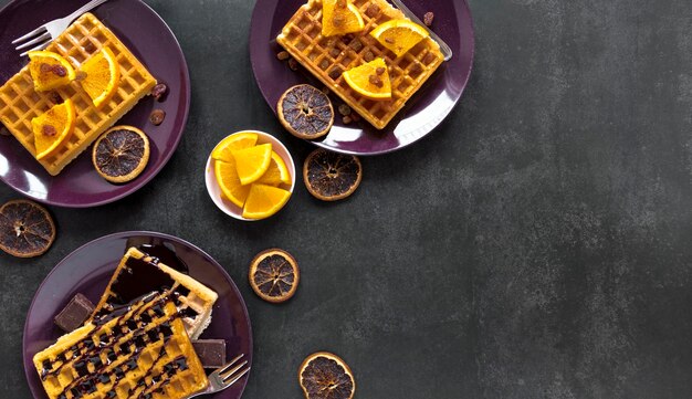 Endecha plana de waffles en platos con chocolate y cítricos.