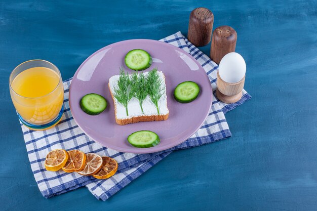 Eneldo en pan de queso junto al pepino en rodajas en un plato junto a los materiales en un paño de cocina en azul.