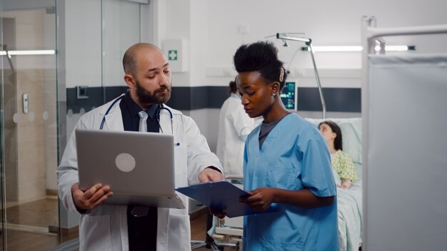 Enfermera africana y médico cirujano en uniforme médico analizando los síntomas de la enfermedad trabajando en la sala del hospital